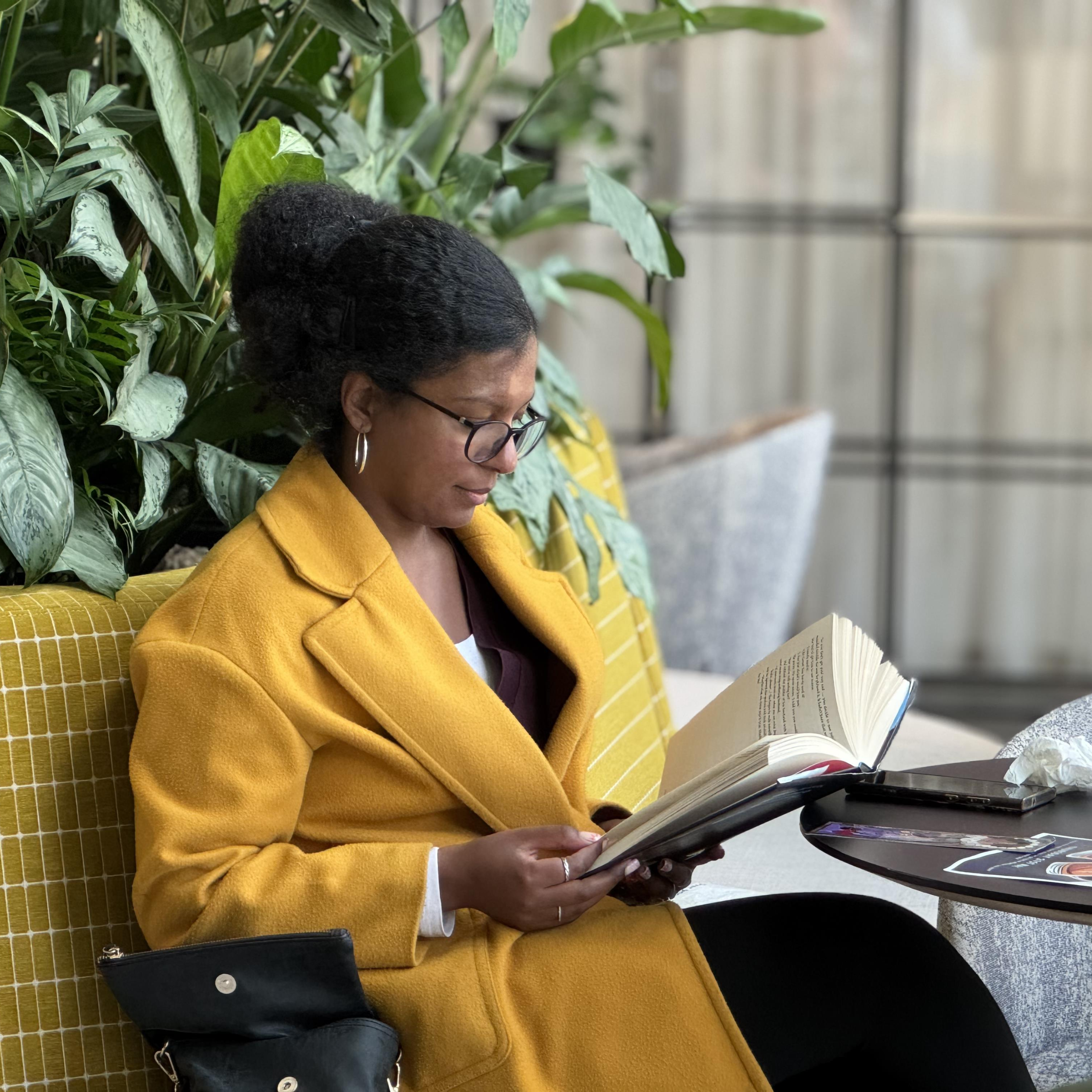 Woman in yellow jacket reading at a table.